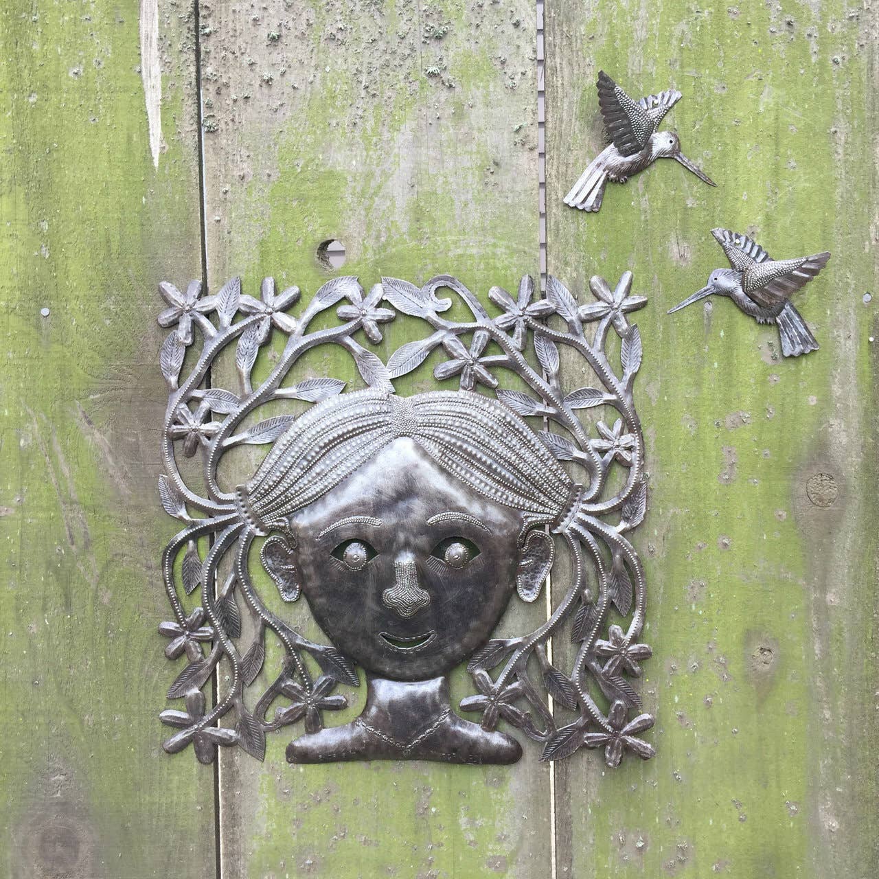Handmade Haitian hammered metal wall art of a young girl with pigtails hanging outside