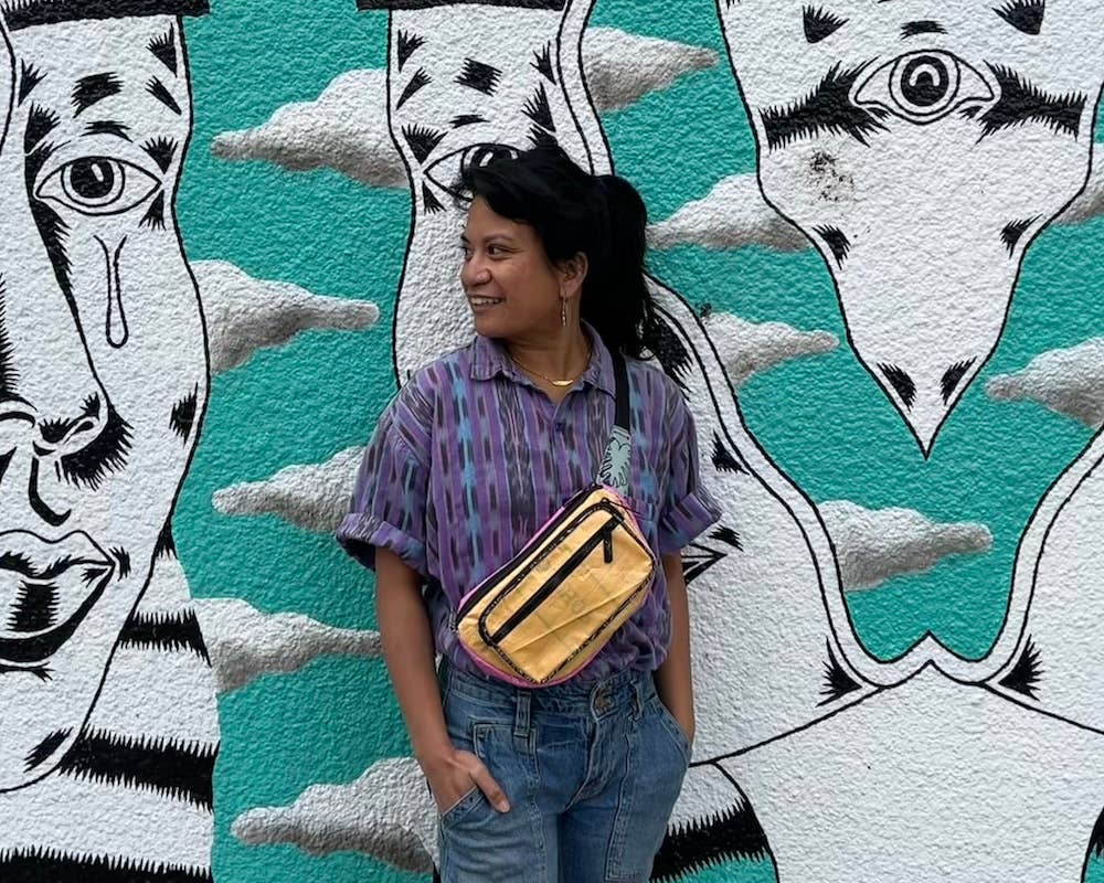 Person wearing the cross body pack. Exterior material is upcycled from feed and cement bags, Interior material is recycled from plastic bottles. Each design is unique.