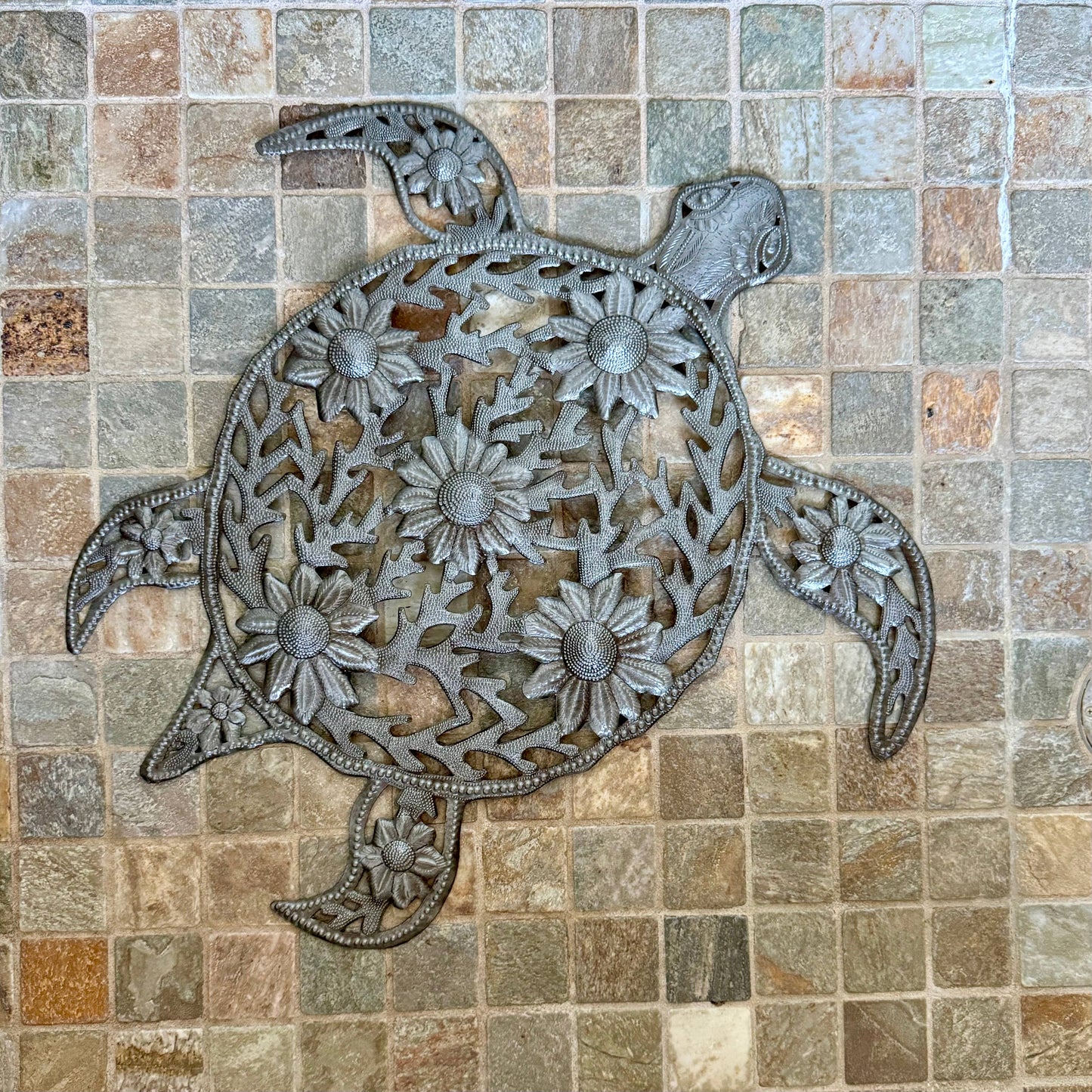 Handmade hammered metal wall art of a turtle with flowers on tile