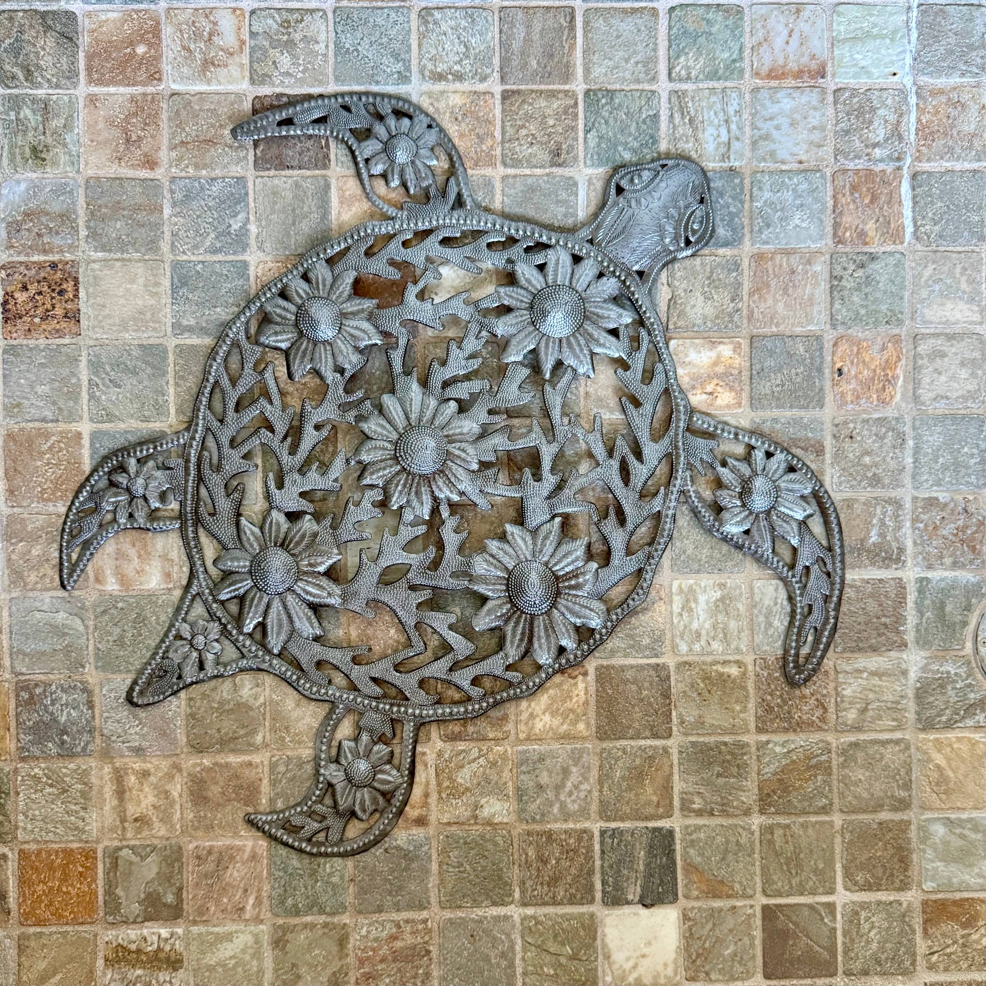 Handmade hammered metal wall art of a turtle with flowers on tile