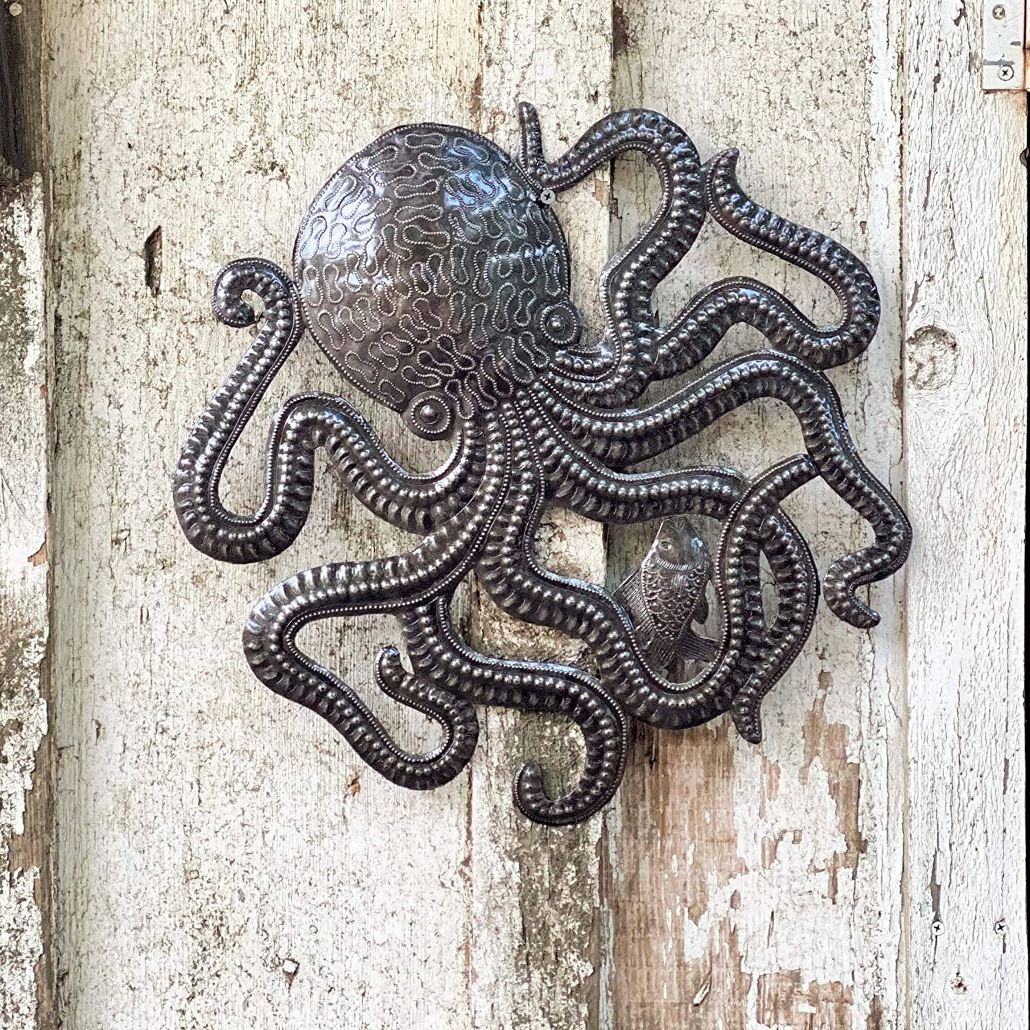 Handmade Haitian hammered metal wall art of an octopus and fish hanging outside hanging outside
