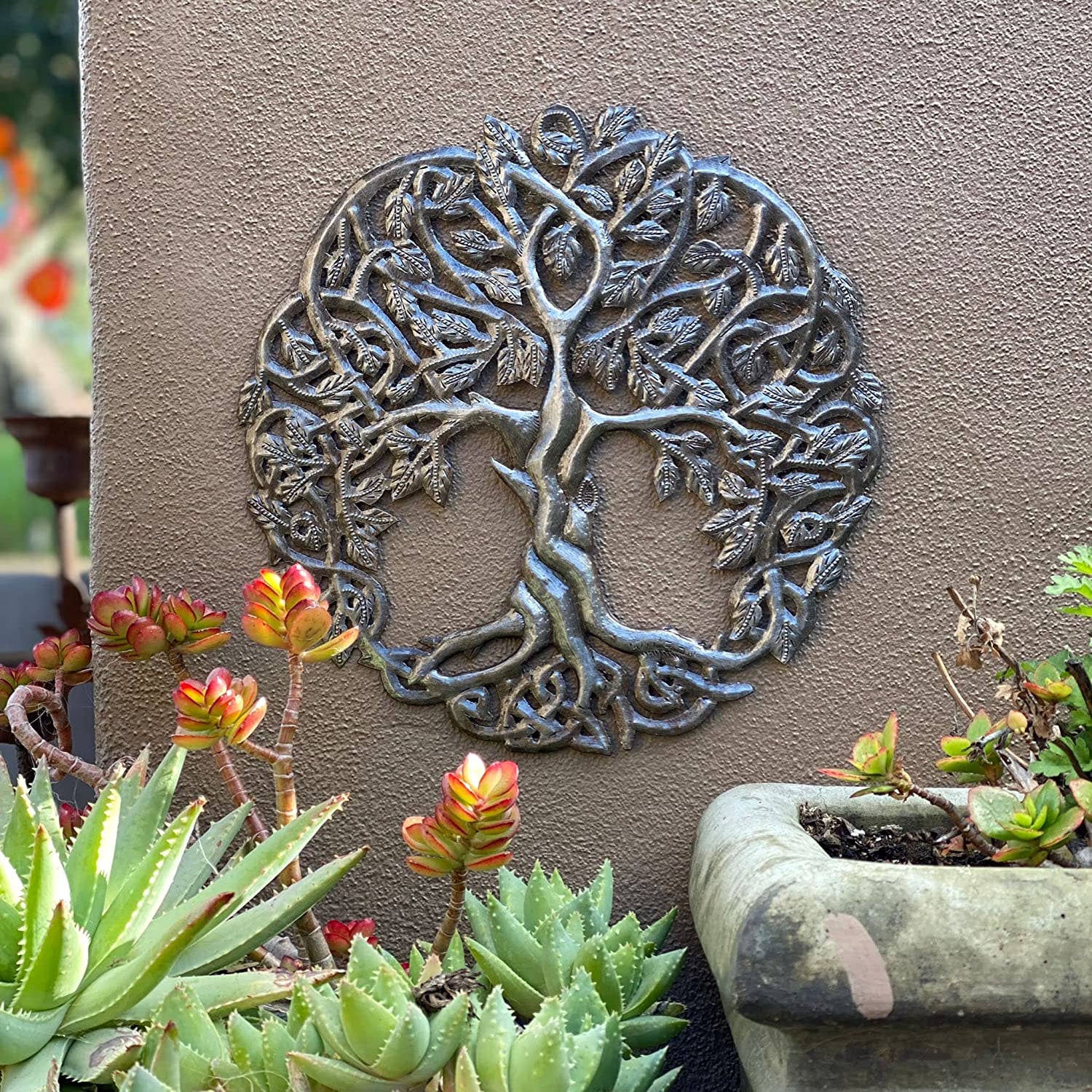 Handmade Haitian hammered metal wall art of a tree with intricate designs on a wall outside.
