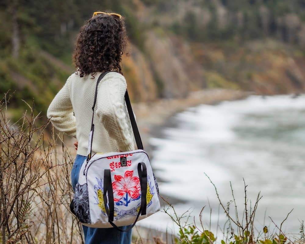 Person wearing a bowler style duffle bag. Exterior material is upcycled from feed and cement bags, Interior material is recycled from plastic bottles. Each design is unique.