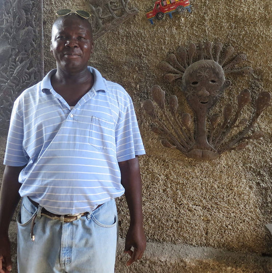 Artist next to the handmade Haitian hammered metal wall art of person's face