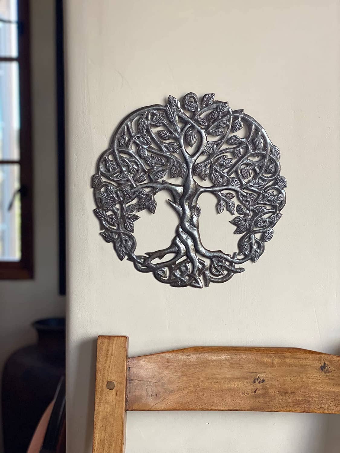Handmade Haitian hammered metal wall art of a tree with intricate designs on a wall indoors.