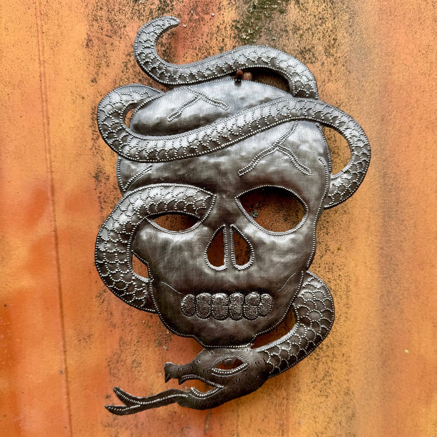Handmade Haitian hammered metal wall art of a skull with a snake entwined
