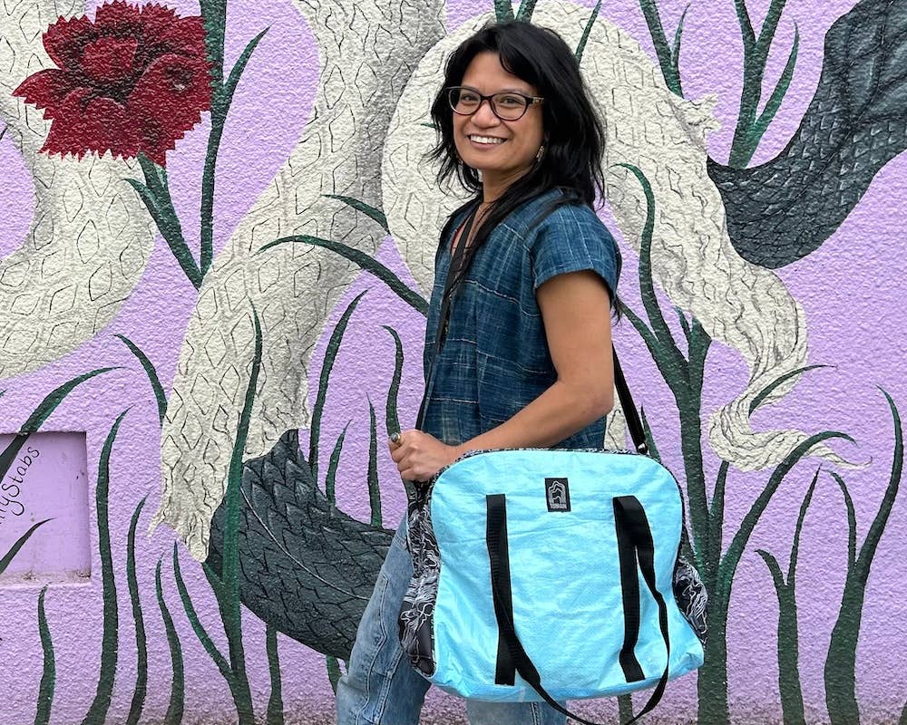 Person wearing the bowler style duffle bag. Exterior material is upcycled from feed and cement bags, Interior material is recycled from plastic bottles. Each design is unique.