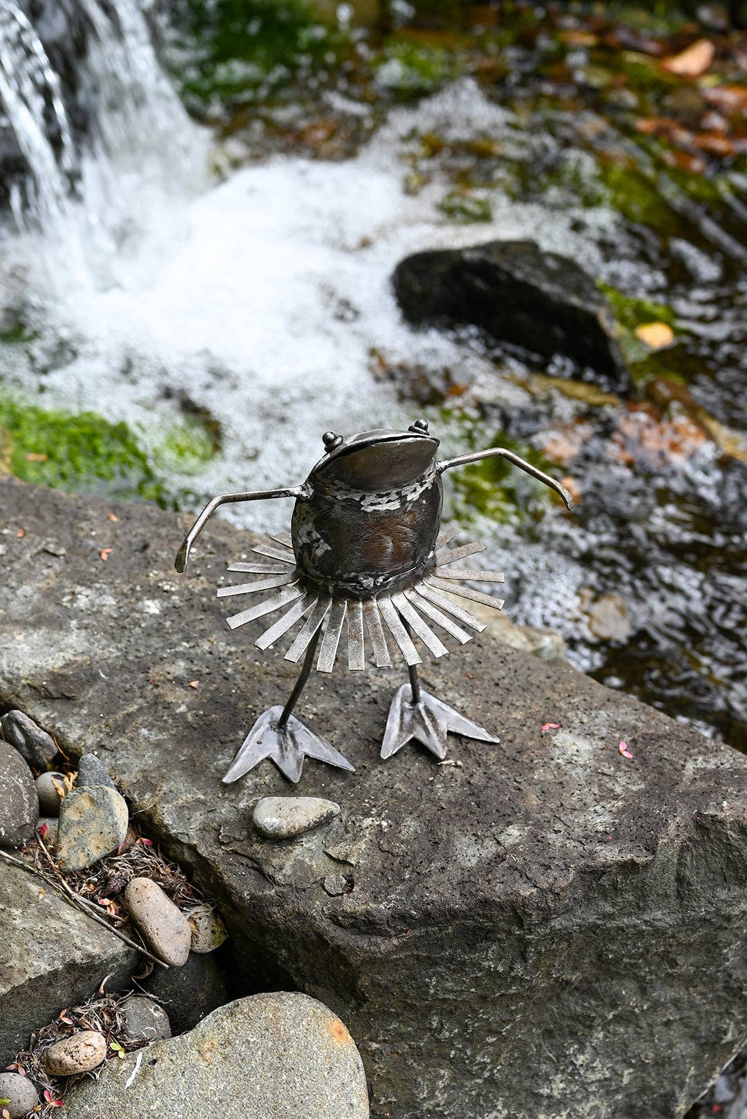Metallic dancing frog with a swirling skirt on a stone by the river.