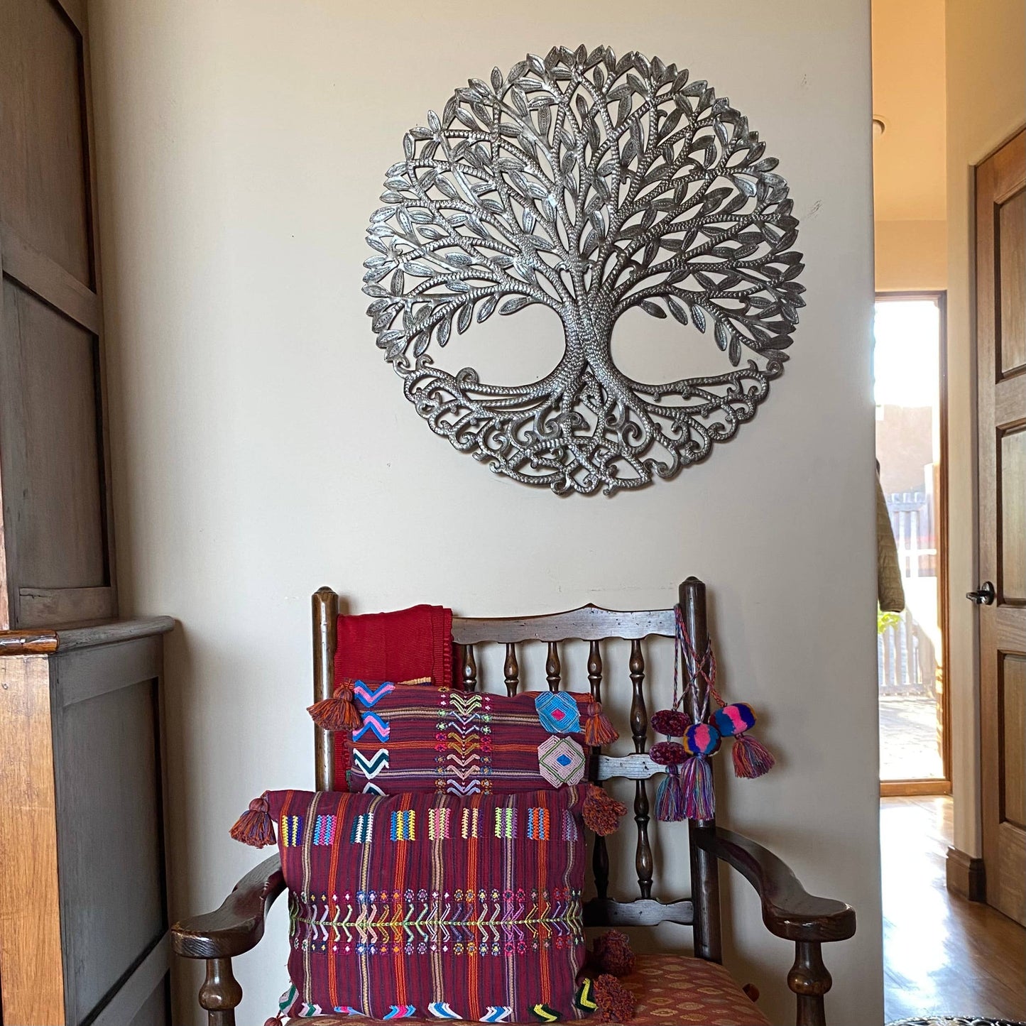 Handmade hammered metal wall art of a tree with intricate designs hanging inside.