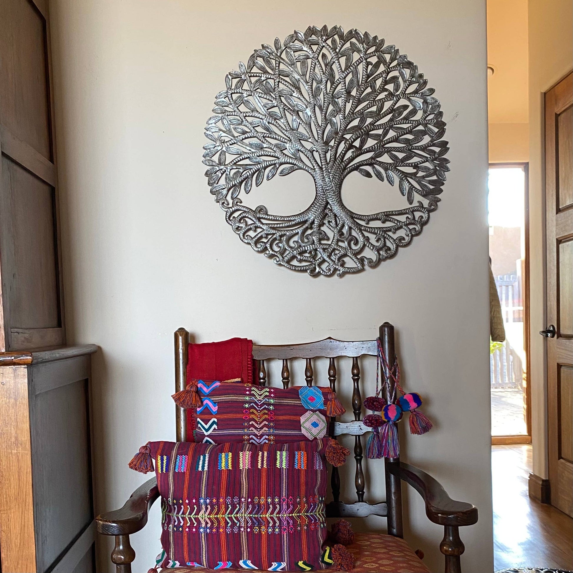 Handmade hammered metal wall art of a tree with intricate designs hanging inside.