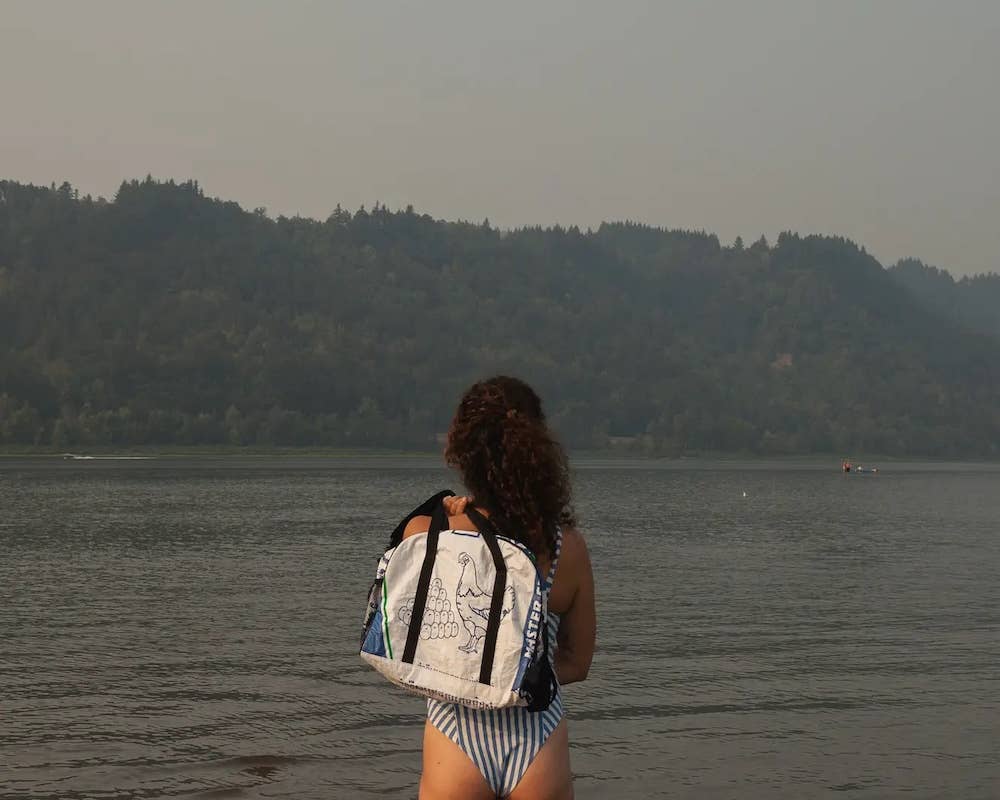 Person holding the bowler style duffle bag. Exterior material is upcycled from feed and cement bags, Interior material is recycled from plastic bottles. Each design is unique.