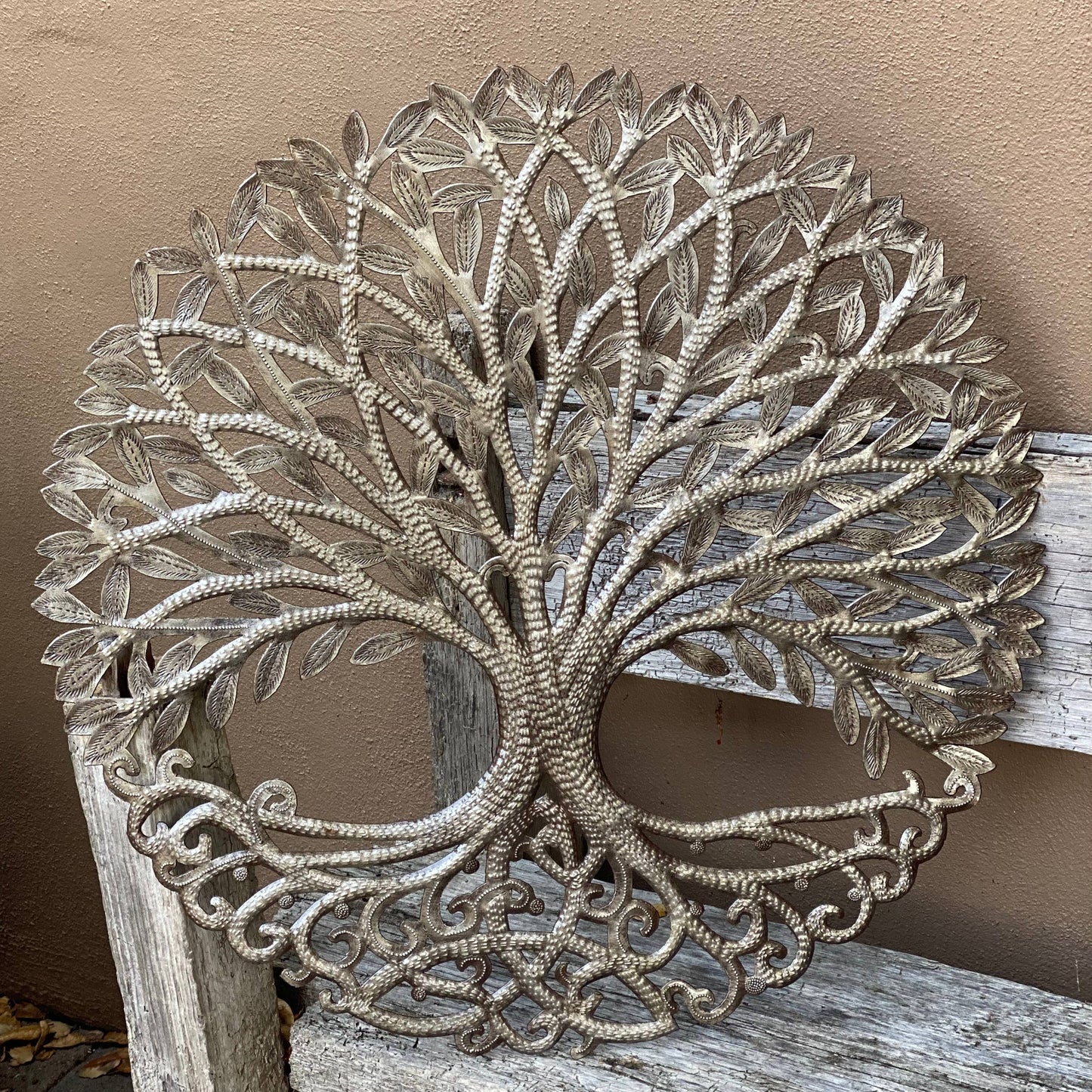 Handmade Haitian hammered metal wall art of a tree with intricate designs outside