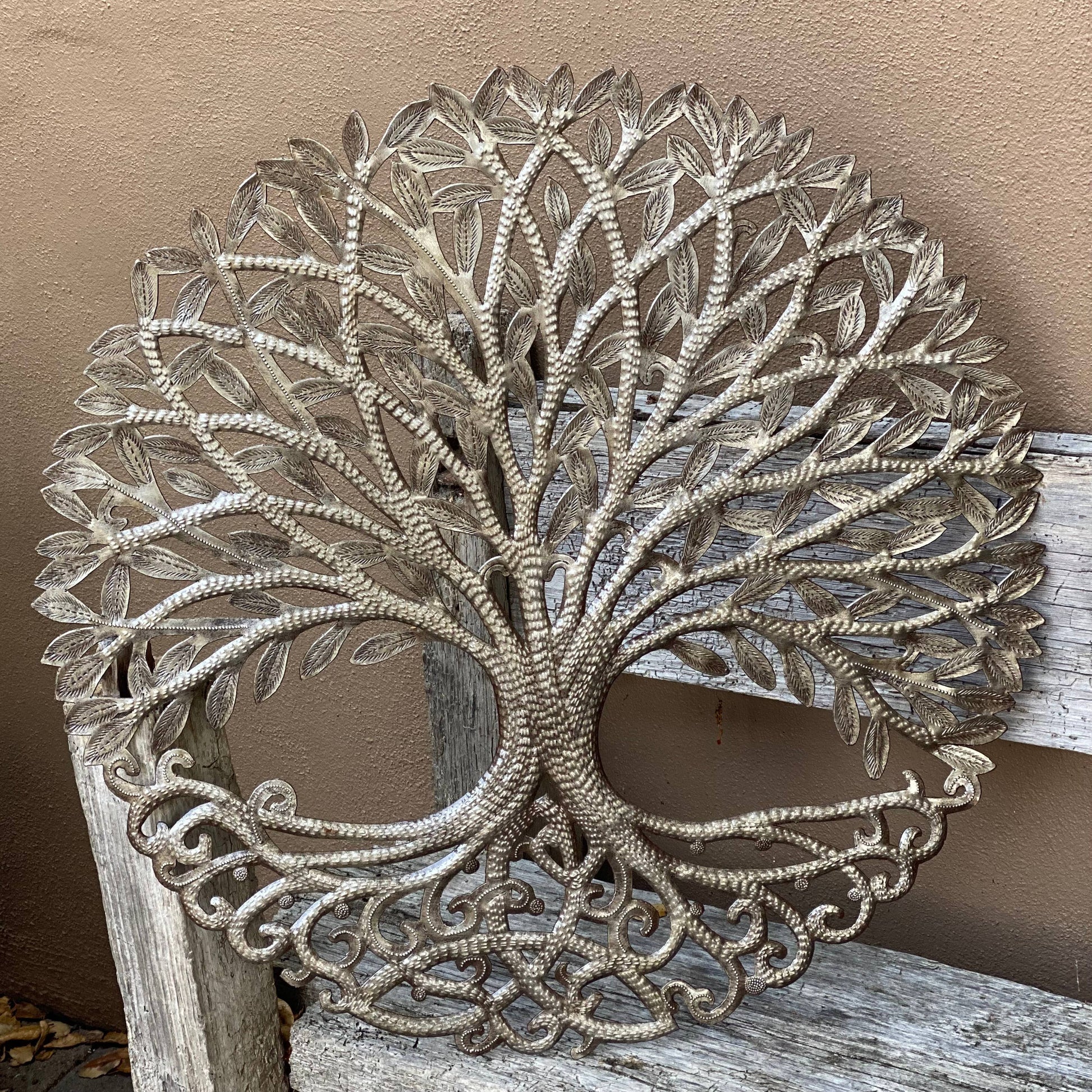 Handmade Haitian hammered metal wall art of a tree with intricate designs outside