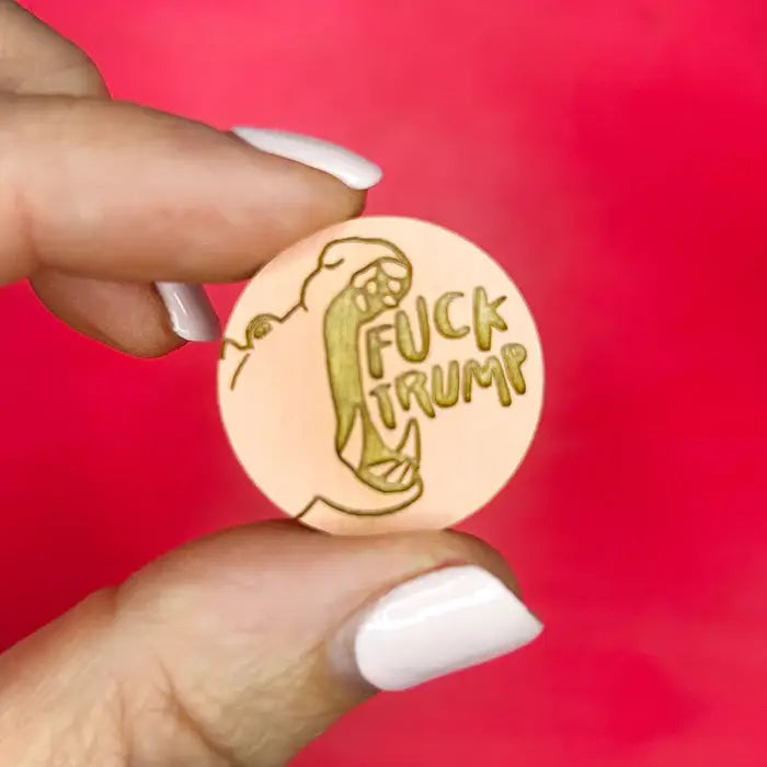 Hand holding a hippo button with 'Fuck Trump' text