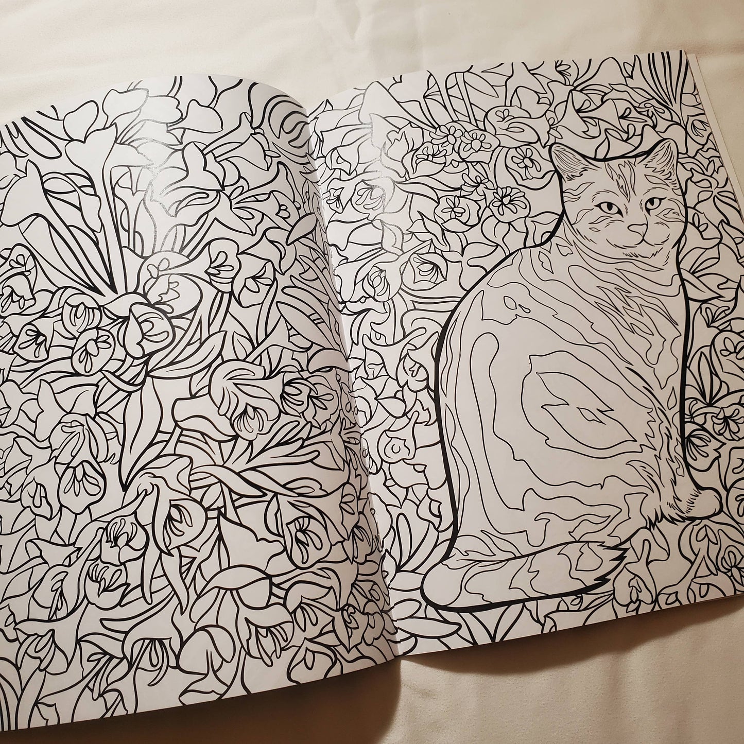 Open coloring book with a cat and floral design on a plain background
