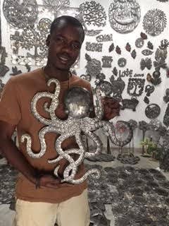 Artist holding the handmade Haitian hammered metal wall art of an octopus