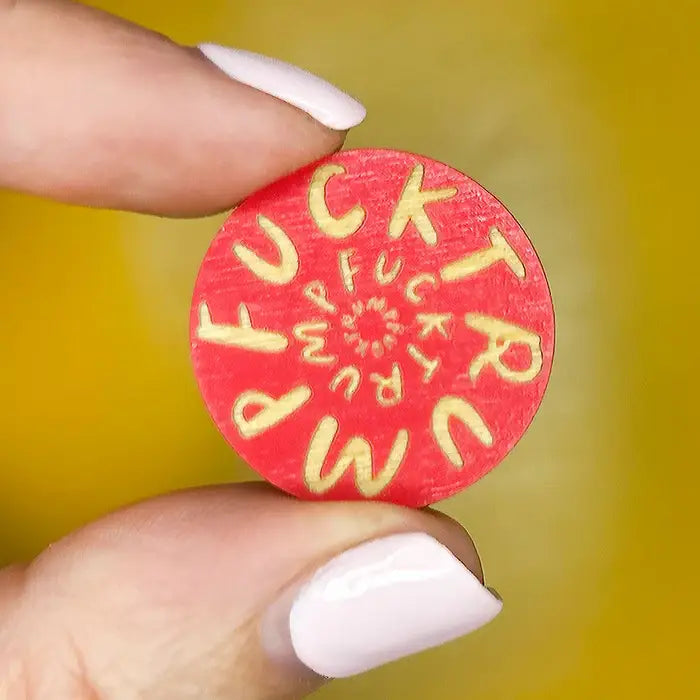 Red circular pin with printed text "Fuck Trump" held by a hand