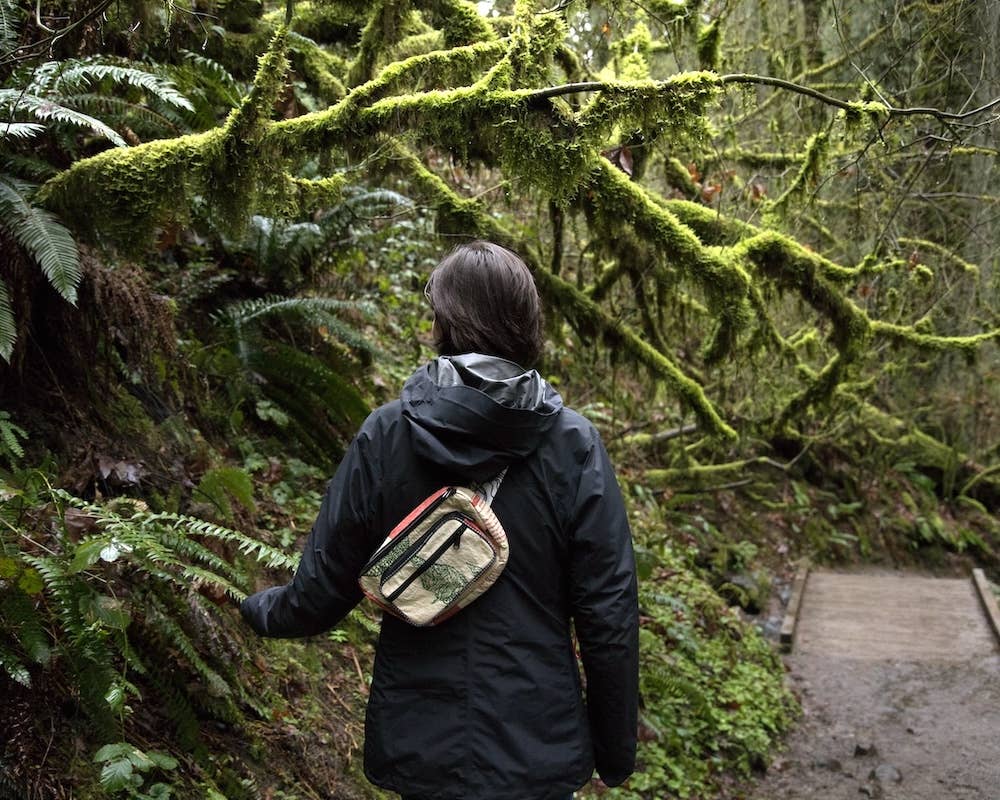 Person wearing the cross body pack. Exterior material is upcycled from feed and cement bags, Interior material is recycled from plastic bottles. Each design is unique.