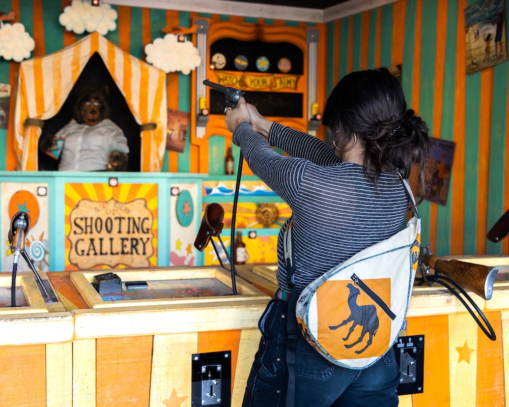 Person wearing a teardrop shaped sling bag. Exterior material is upcycled from feed and cement bags, Interior material is recycled from plastic bottles. Each design is unique.