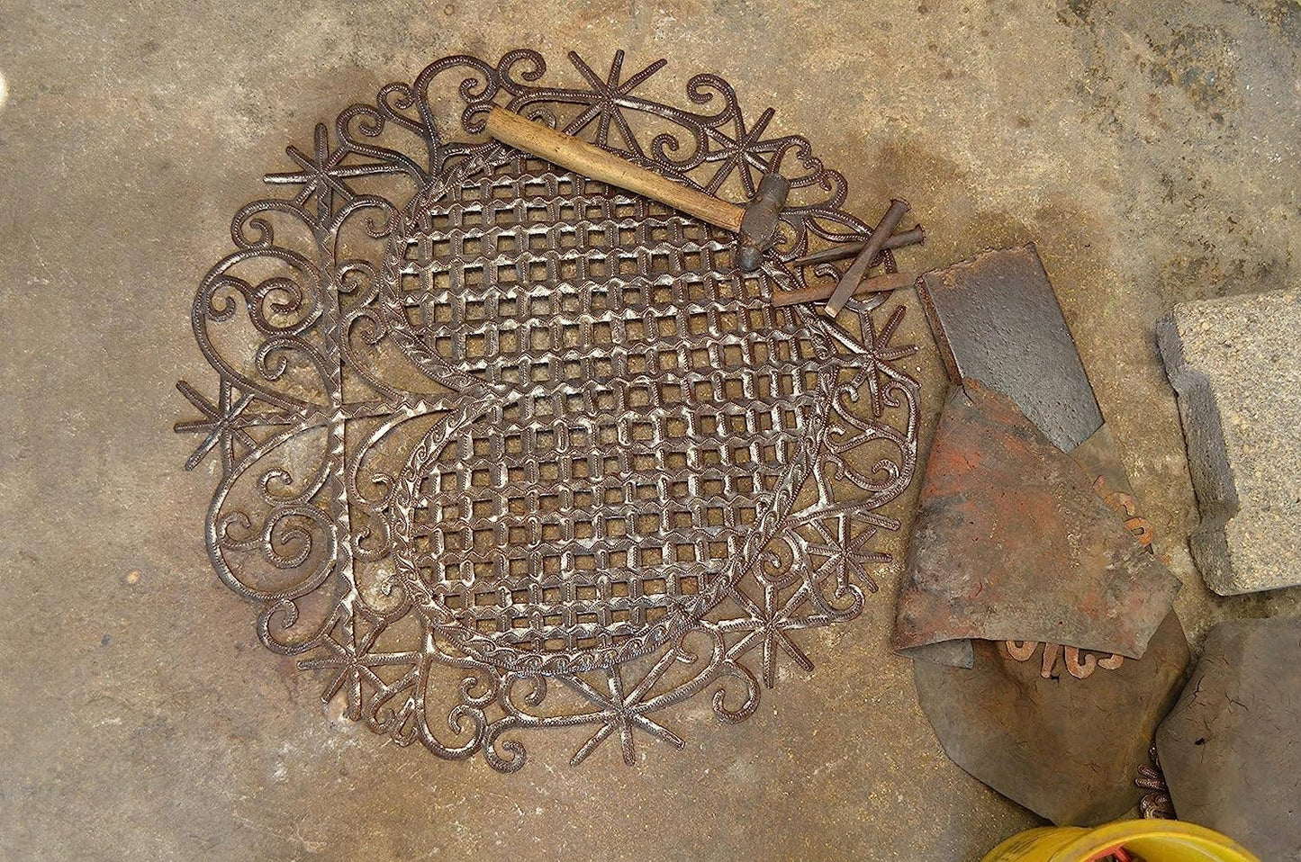 Handmade Haitian hammered metal wall art of a heart in an artist's workshop.