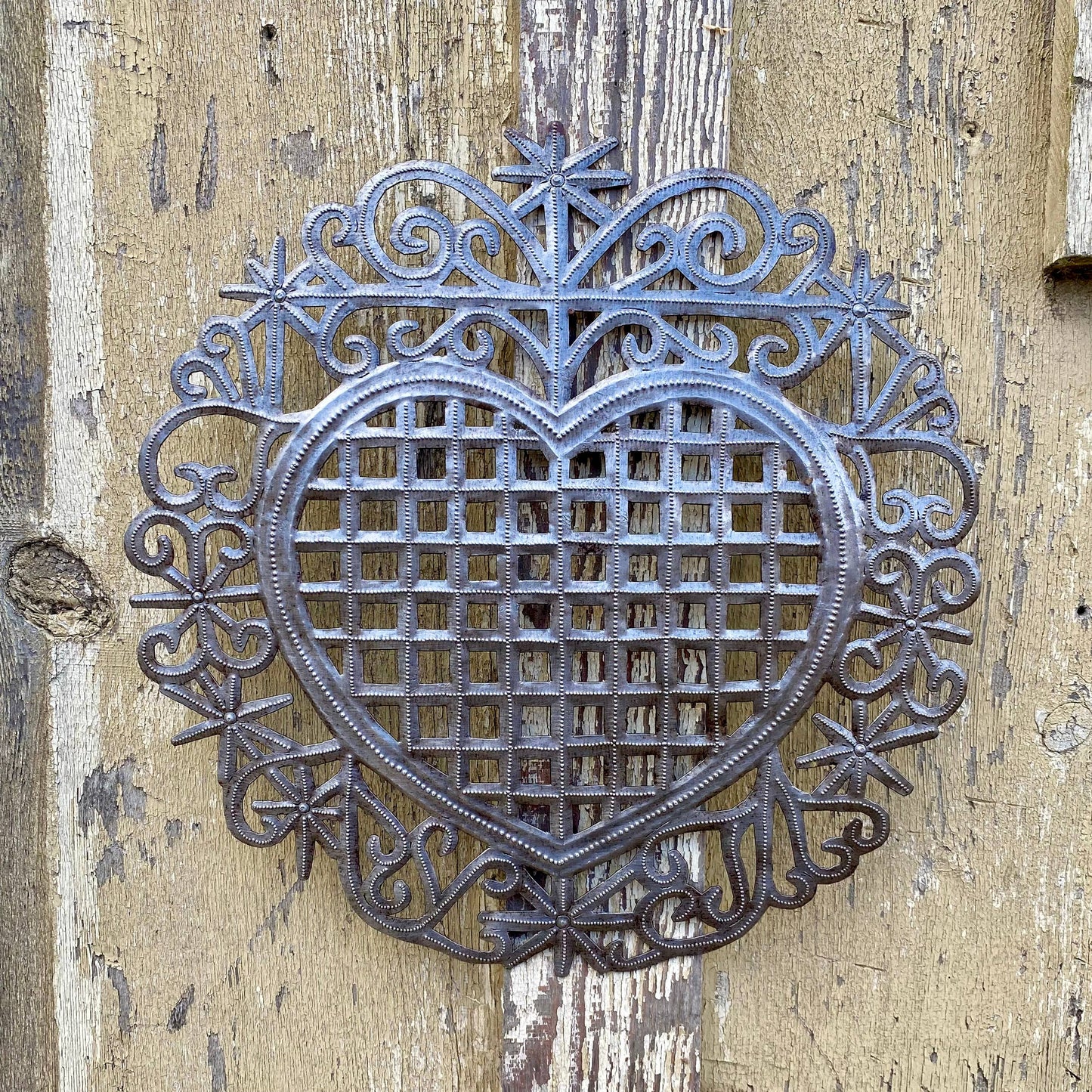 Handmade Haitian hammered metal wall art of a heart hanging outside.
