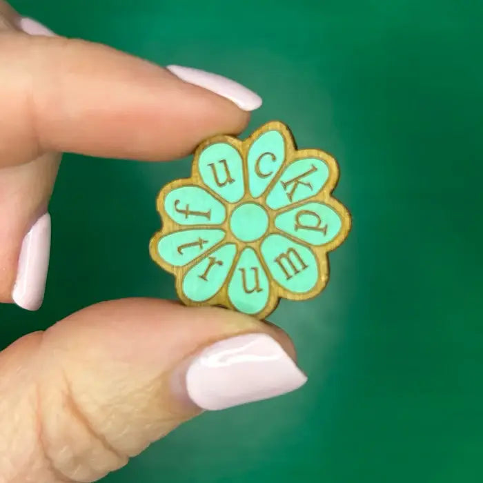 Floral-shaped pin with text held by a hand reading "Fuck Trump"