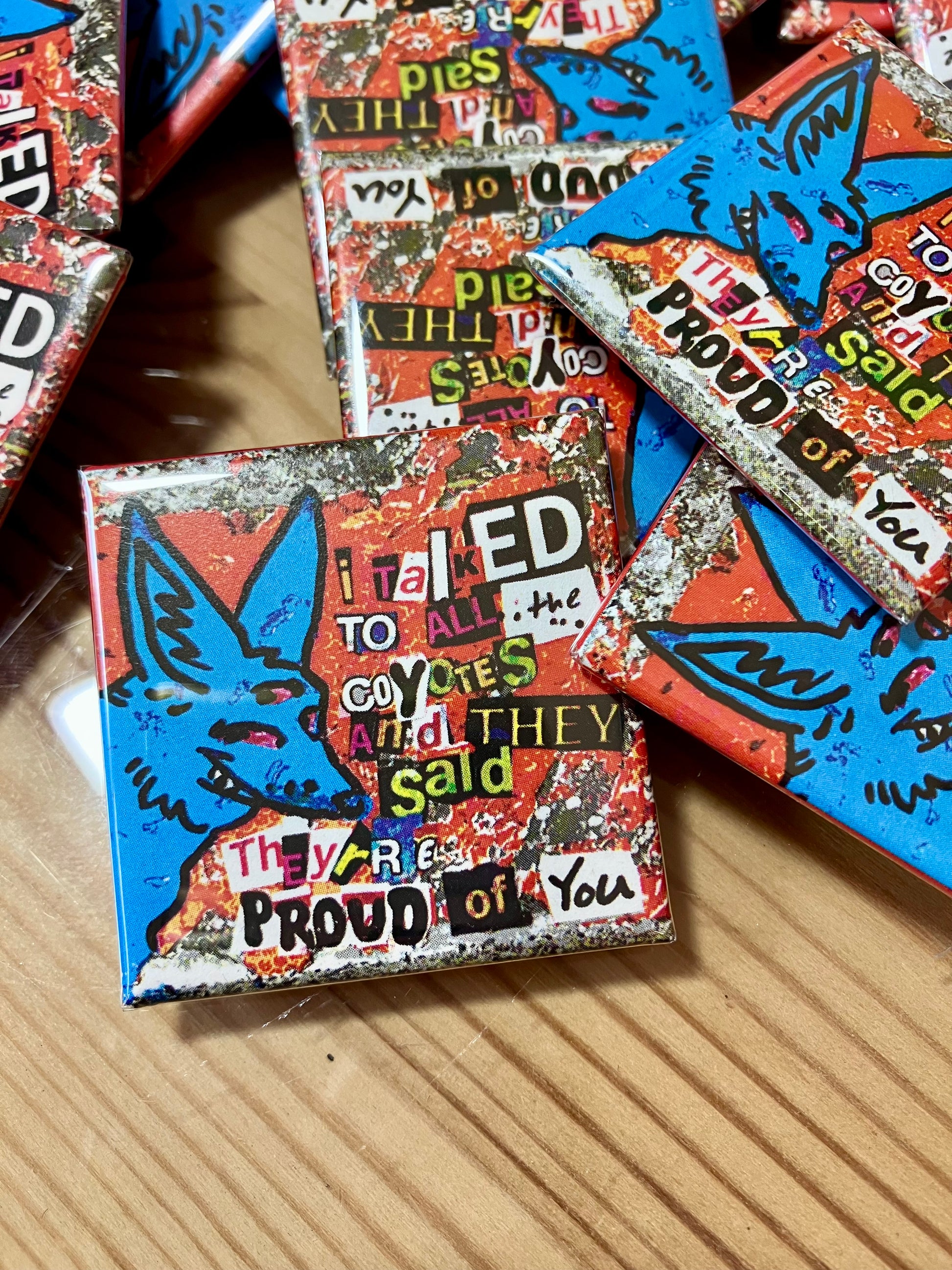 Pins of a three eyed blue coyote that reads "I talked to all the coyotes and they said they're proud of you" using a ransom note-esk font