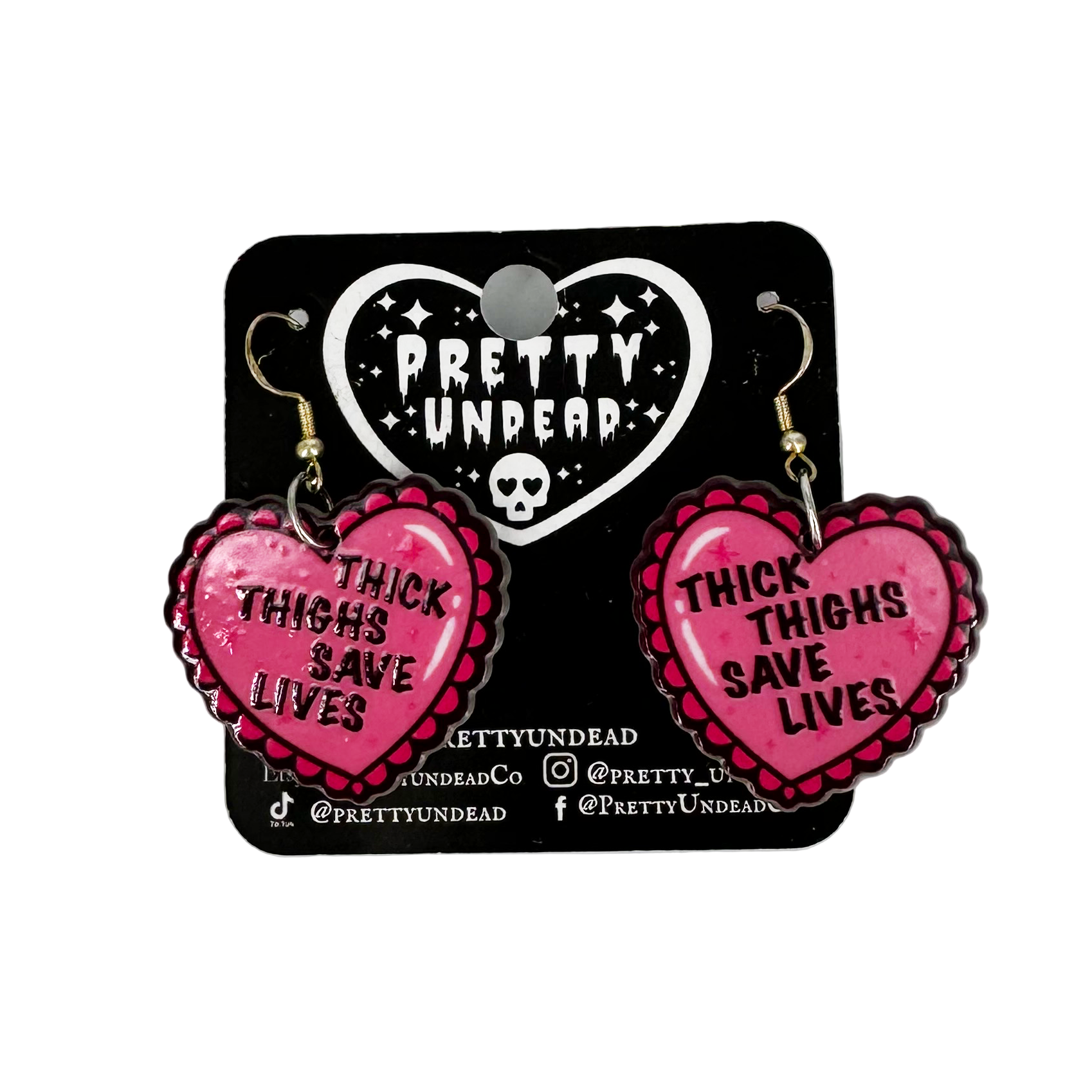 Pink heart-shaped earrings with 'Thick Thighs Save Lives' text on a Pretty Undead branded card.
