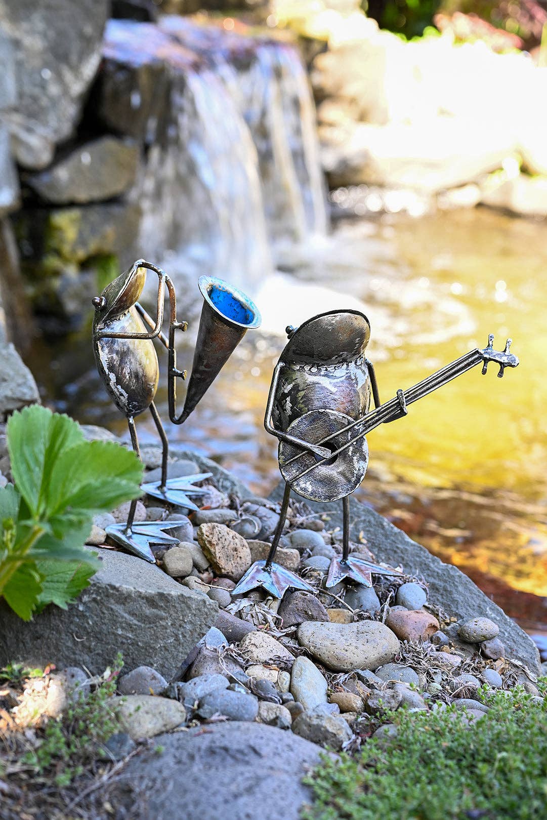Two metallic frogs standing by the river, one playing the horn, the other a banjo.