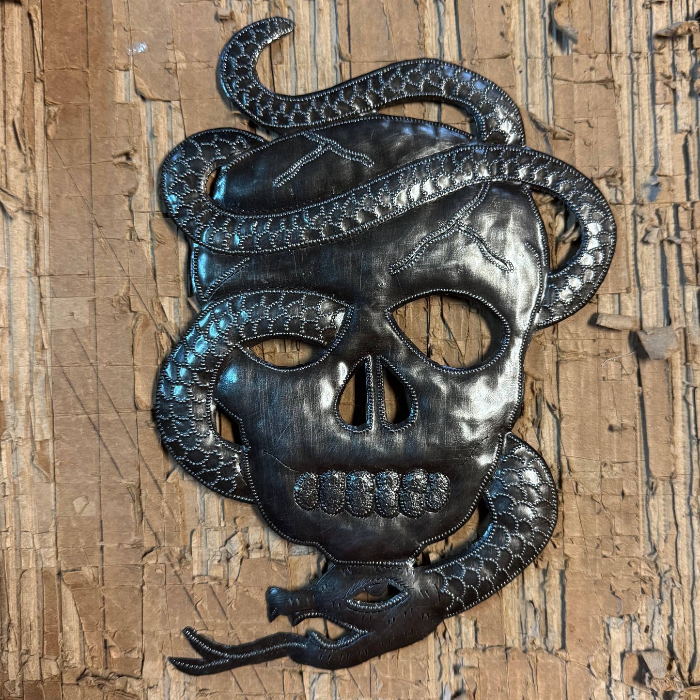 Handmade Haitian hammered metal wall art of a skull with a snake entwined