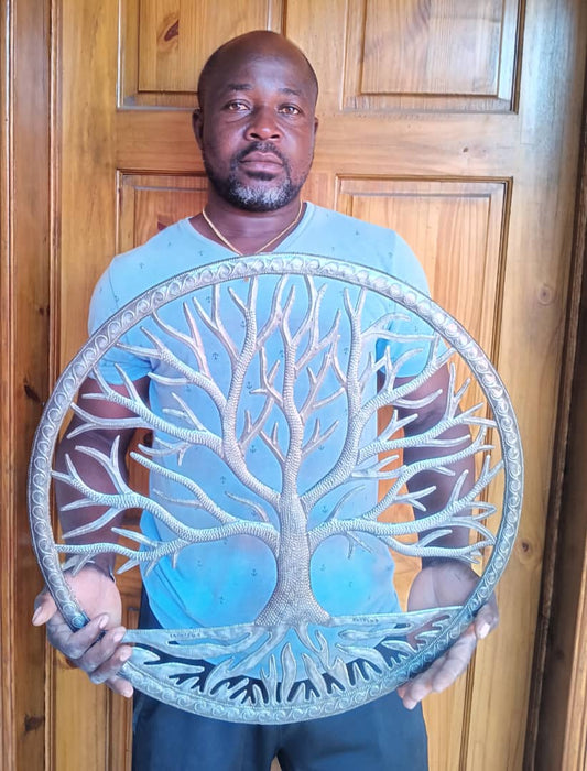 Artist holding the handmade Haitian hammered metal wall art of a tree