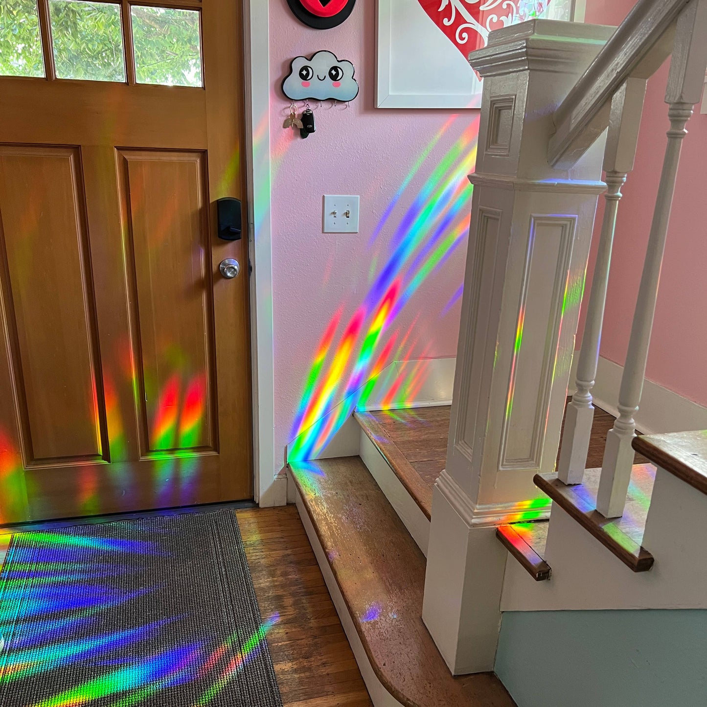 Rainbow light projection on a wooden door and staircase inside a house by the suncatcher decal.