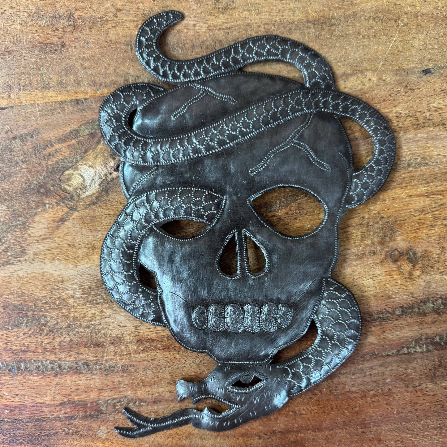 Handmade Haitian hammered metal wall art of a skull with a snake entwined