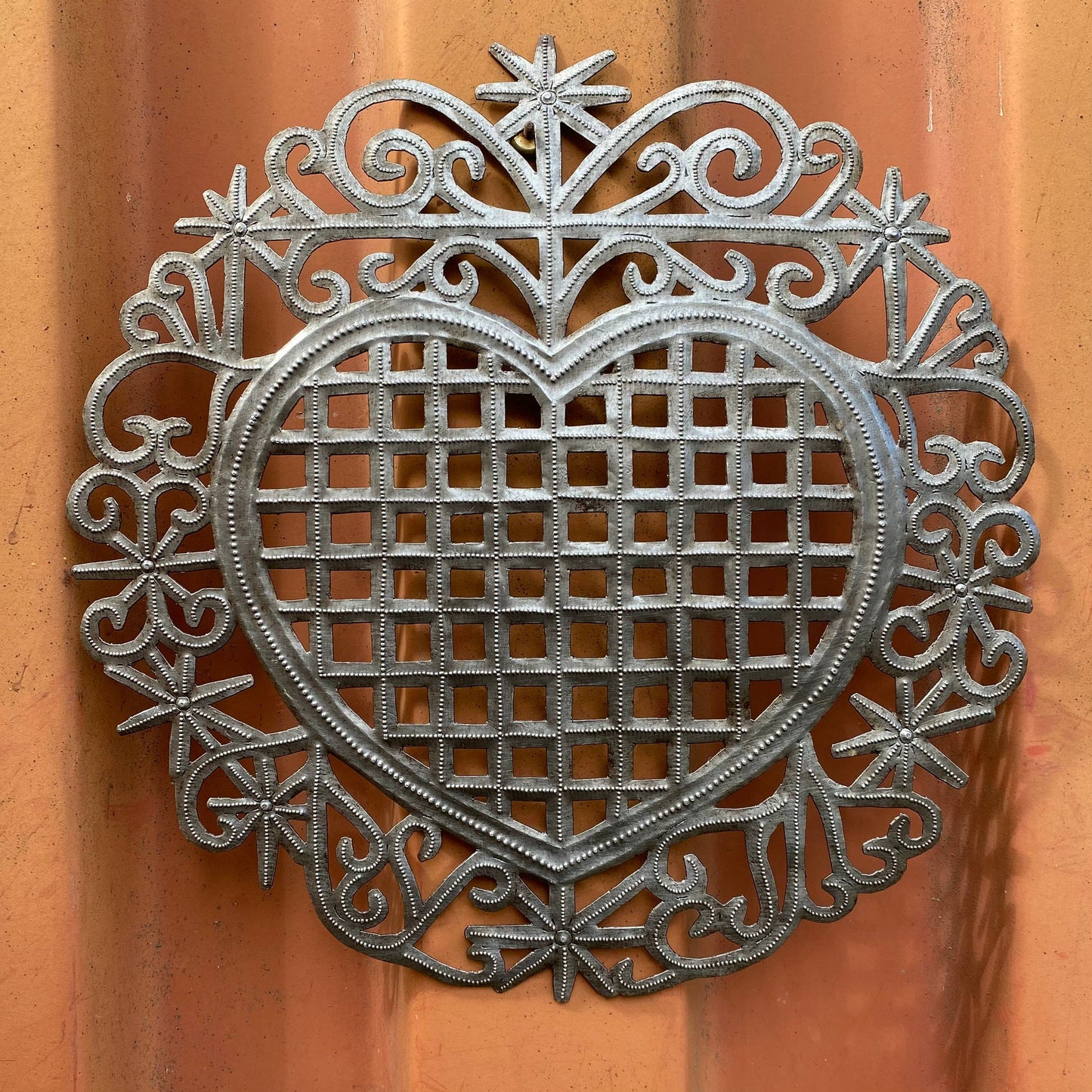 Handmade Haitian hammered metal wall art of a heart hanging inside.