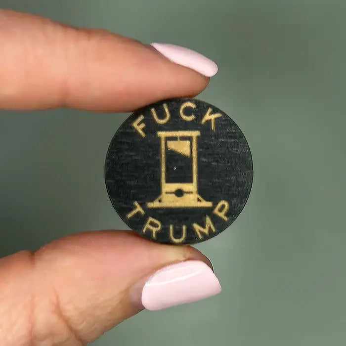 Round black object with 'Fuck Trump' text held by a hand