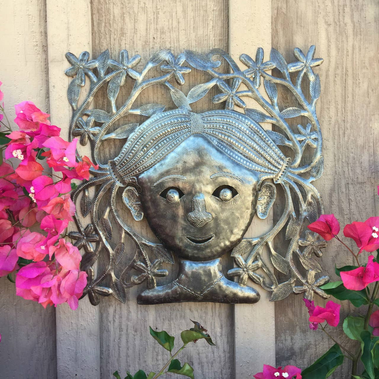 Handmade Haitian hammered metal wall art of a young girl with pigtails hanging outside
