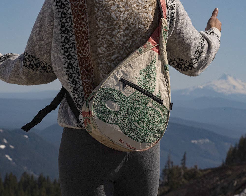 Person wearing  a teardrop shaped sling bag. Exterior material is upcycled from feed and cement bags, Interior material is recycled from plastic bottles. Each design is unique.
