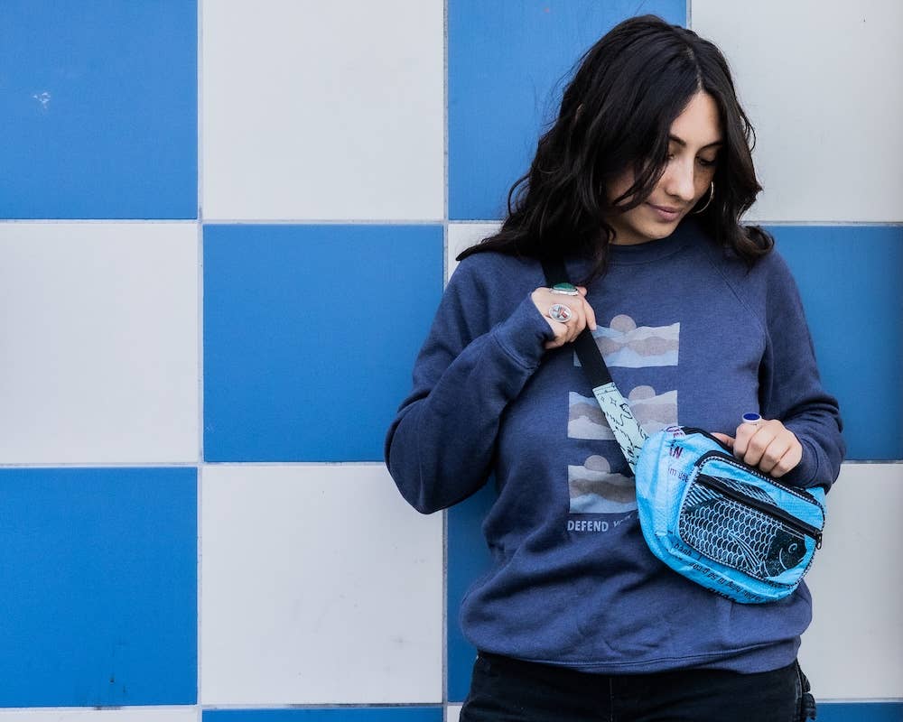 Person wearing the cross-body pack. Exterior material is upcycled from feed and cement bags, Interior material is recycled from plastic bottles. Each design is unique.