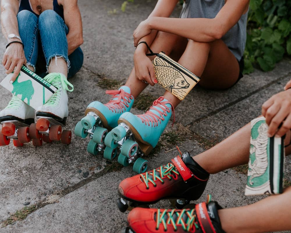Feet of three roller skaters holding a pouch a piece. Exterior material is upcycled from feed and cement bags, Interior material is recycled from plastic bottles. Each design is unique.