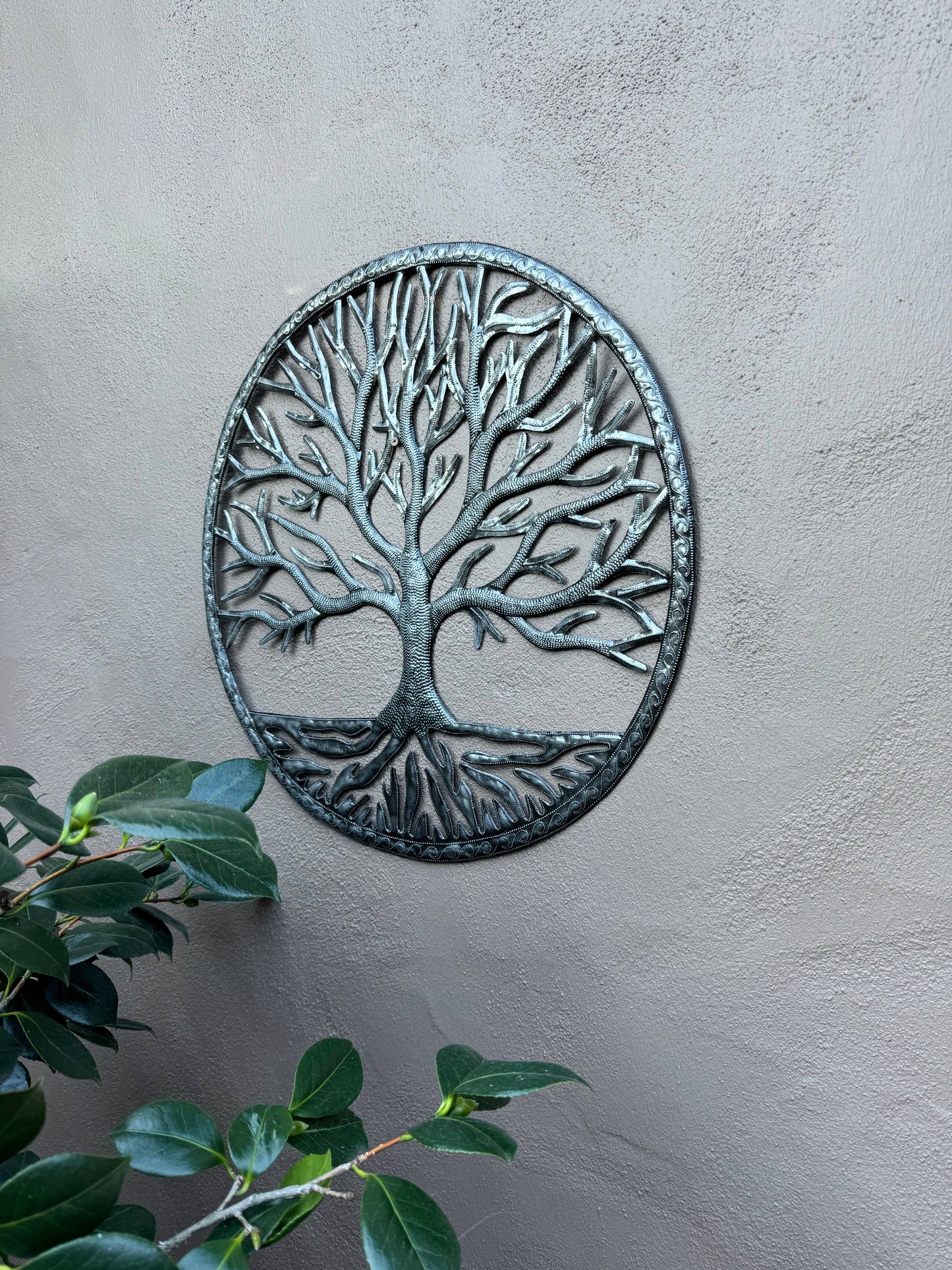 Handmade Haitian hammered metal wall art of a tree hanging outside