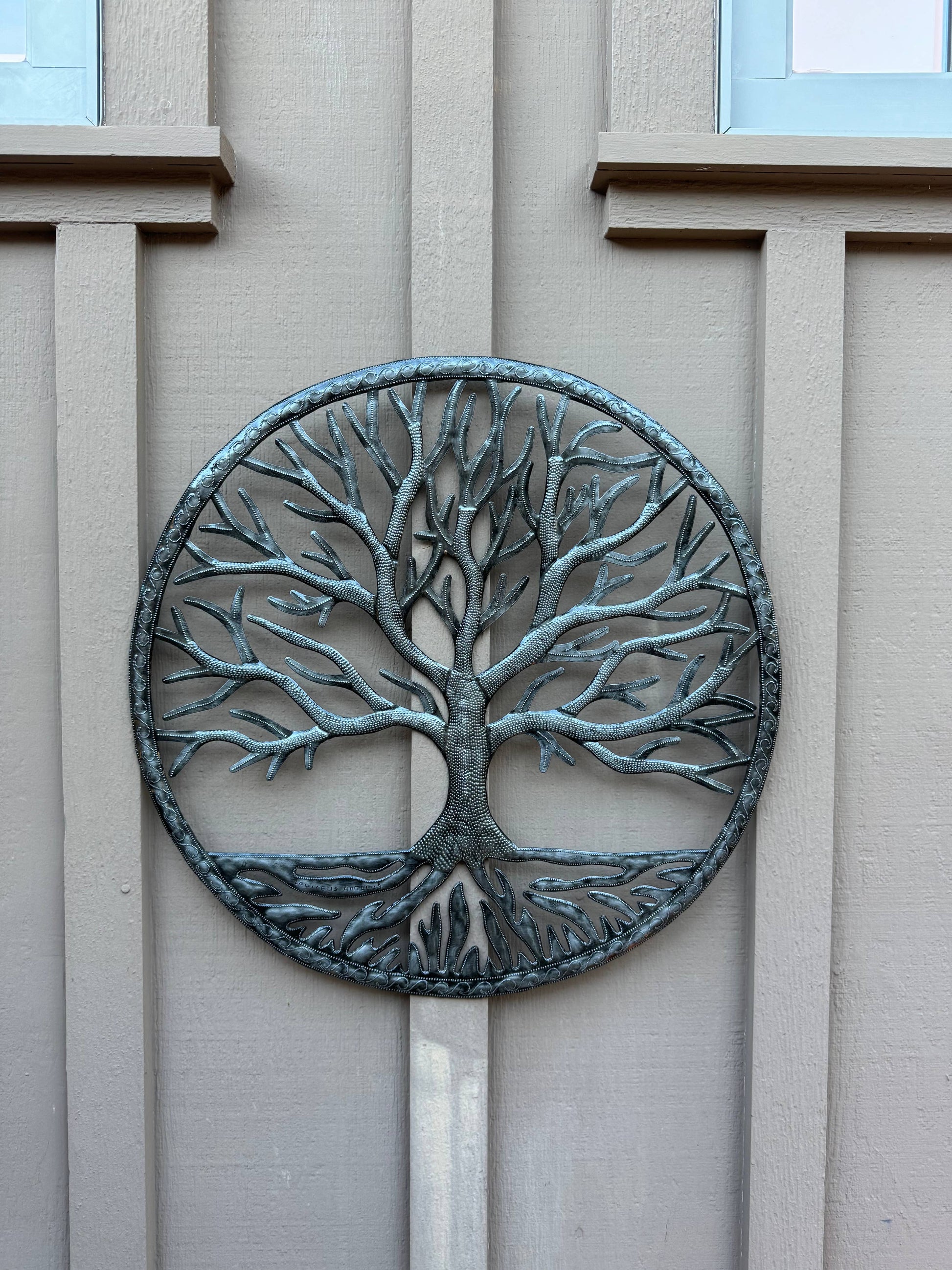Handmade Haitian hammered metal wall art of a tree hanging outside